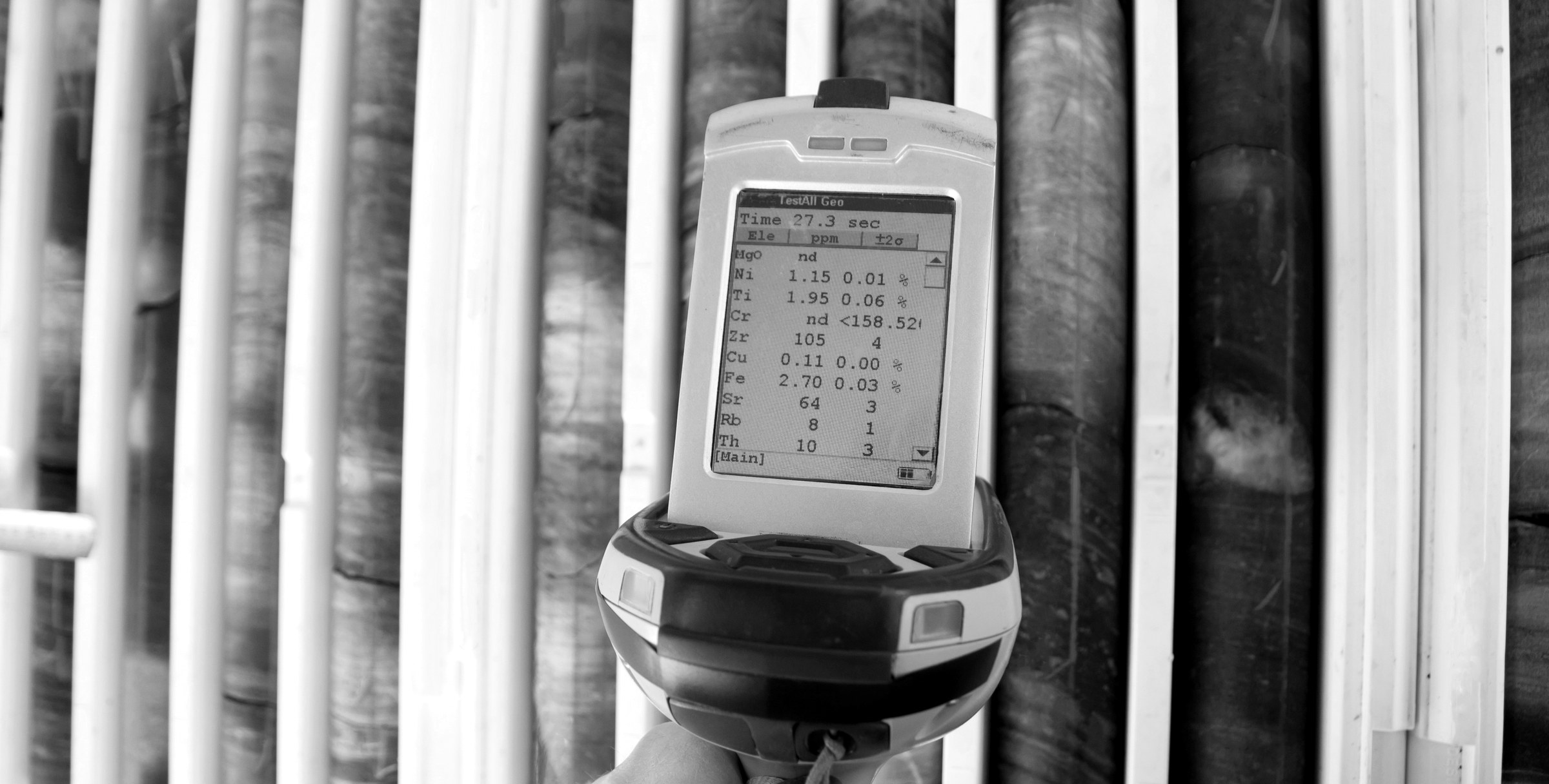 Handheld XRF analyser held over drill core, black and white